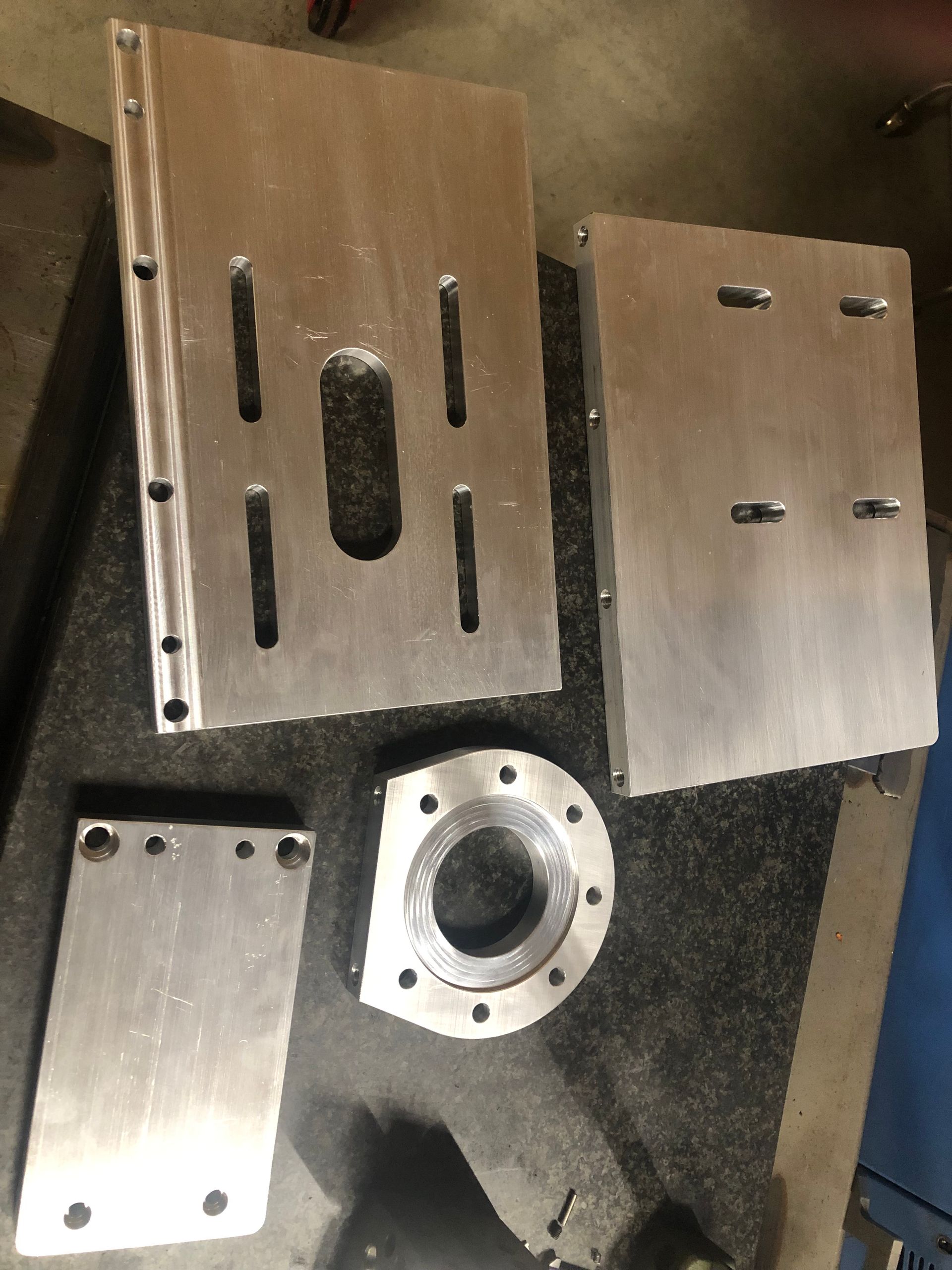 Assorted silver metal plates and a circular flange laid out on a dark work surface.