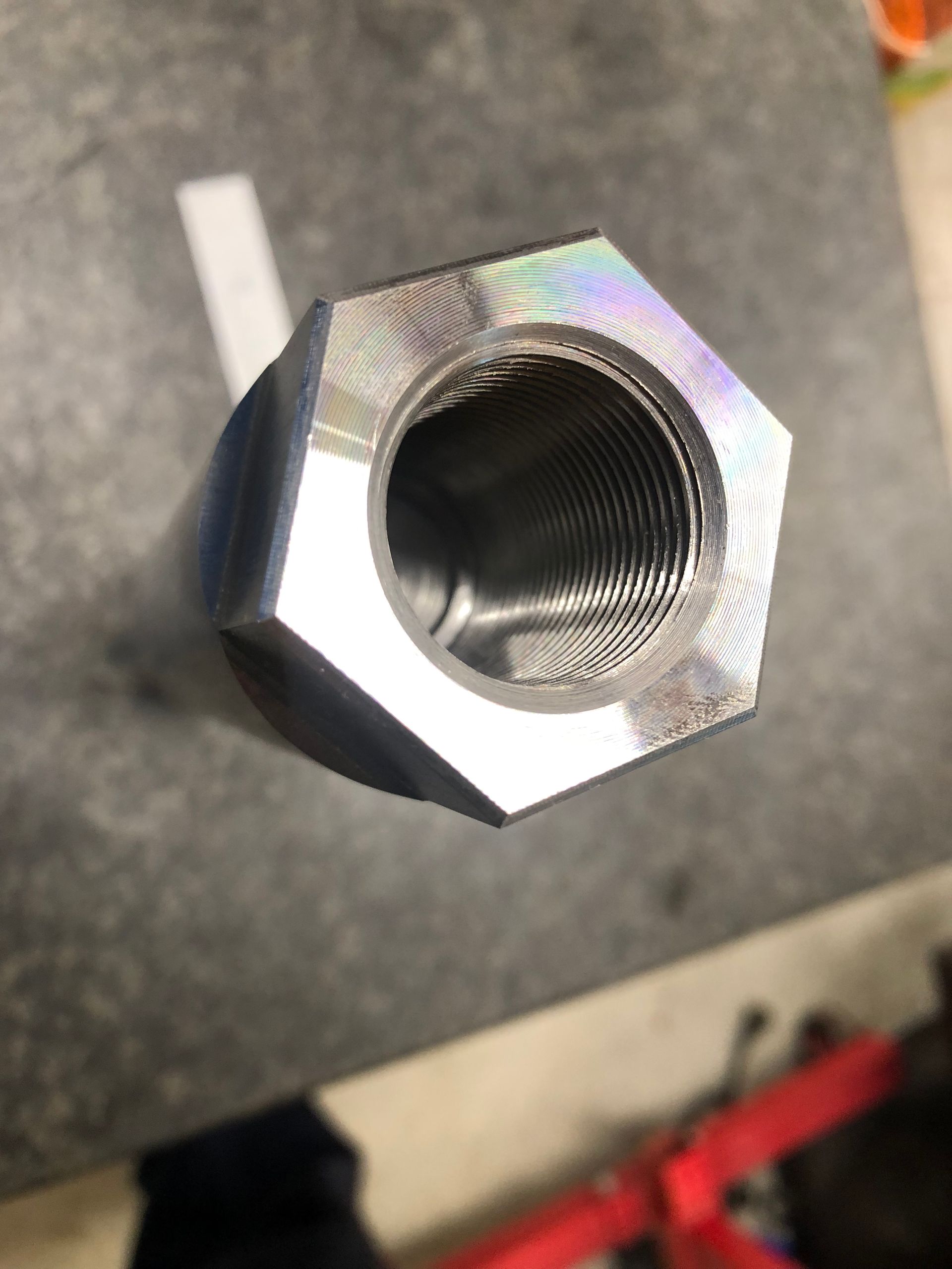 Close-up of a shiny hex nut with threaded interior on a dark work surface.
