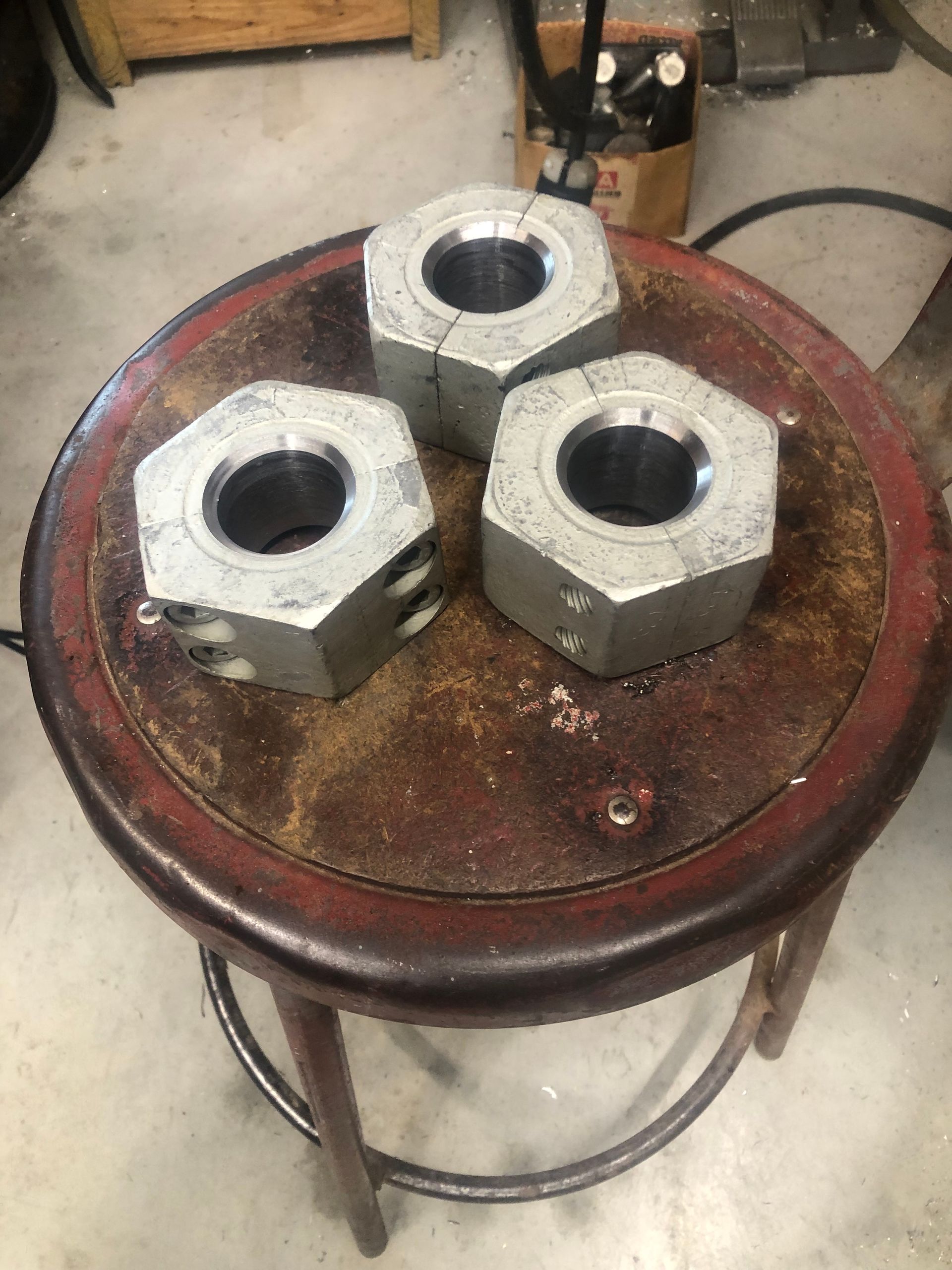 Three large hex nuts on a round wooden stool in a workshop.