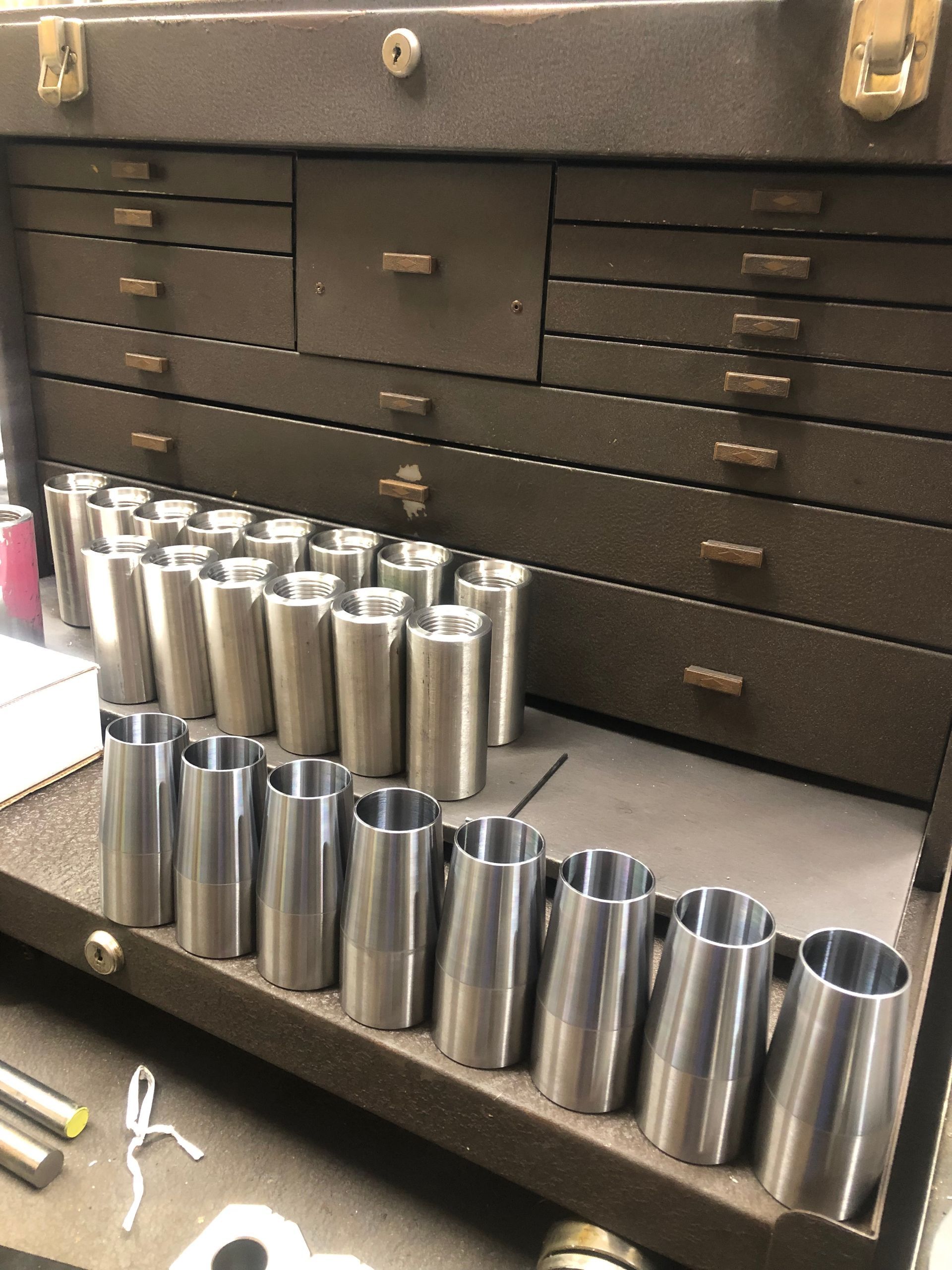 Stainless steel tumblers and tools arranged on a workbench in a garage or workshop.
